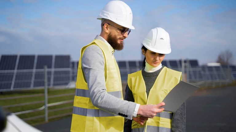 Two engineers in safety gear reviewing plans at a solar farm Two engineers in safety gear reviewing plans at a solar farm