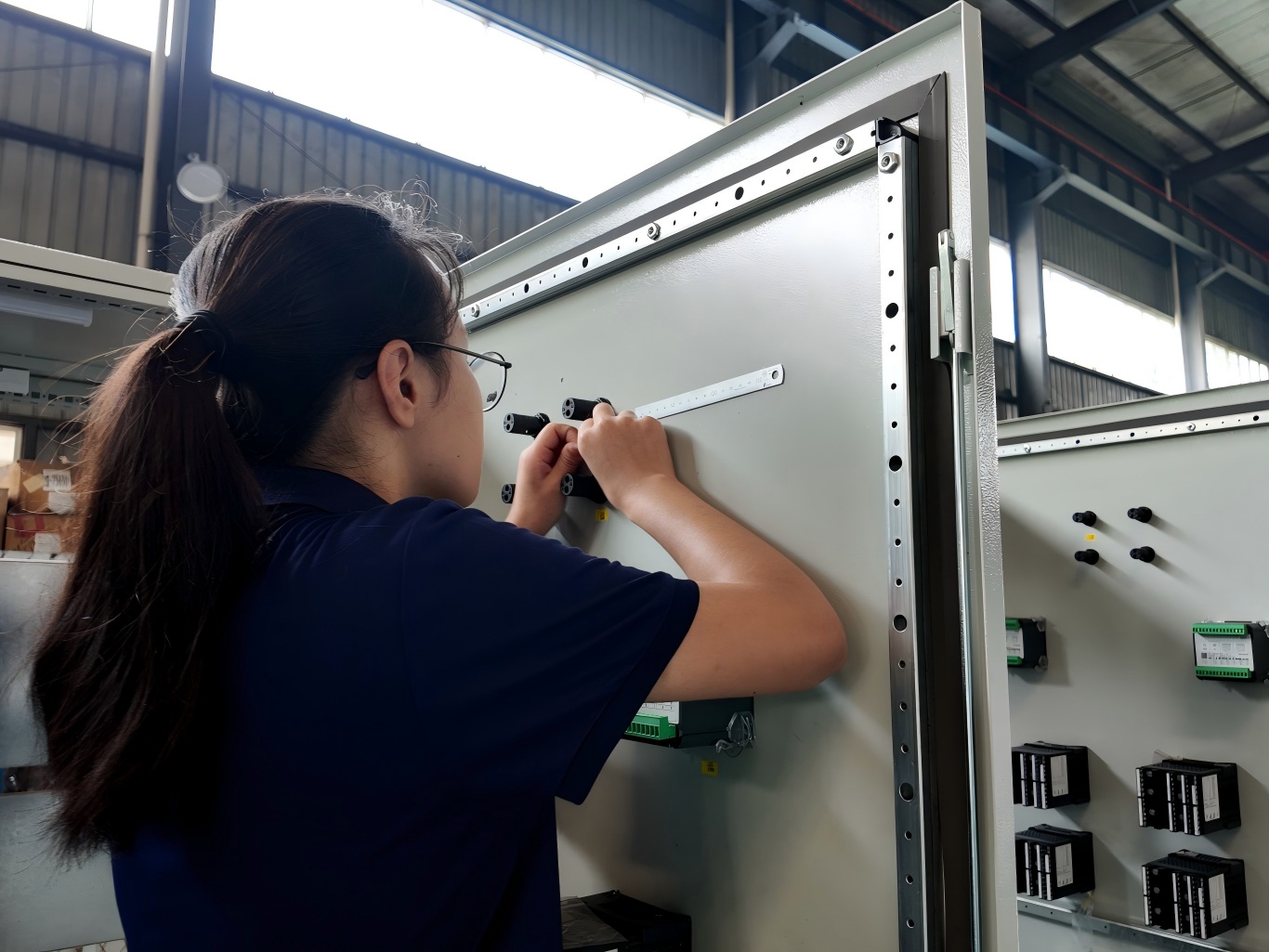 Female worker installing components on industrial electrical control cabinet in workshop