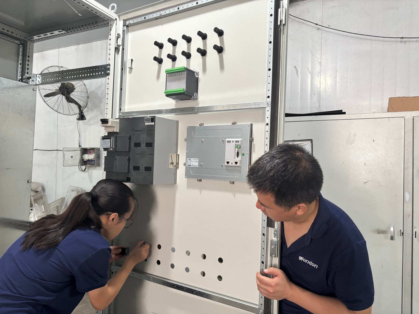Workers assembling industrial temperature control cabinet in factory workshop